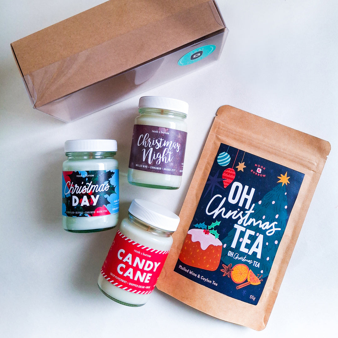 Festive flatlay of four mini candles—“Christmas Day,” “Christmas Night,” “Candy Cane,” and “Oh, Christmas Tea”—with a gift box and tea pouch.