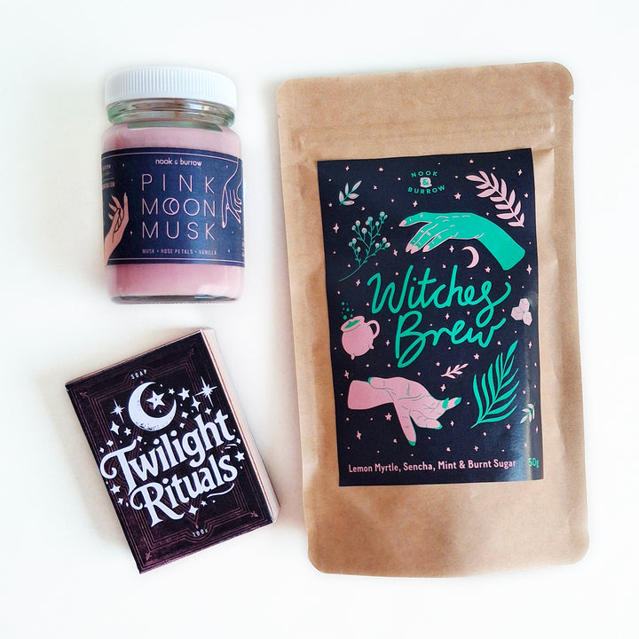 Magical gift set featuring “Witches Brew” tea, “Pink Moon Musk” candle, and “Twilight Rituals” soap, styled with bold, mystical packaging.