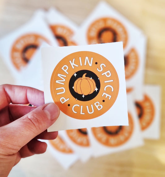 A hand holding an orange Pumpkin Spice Latte Club Sticker