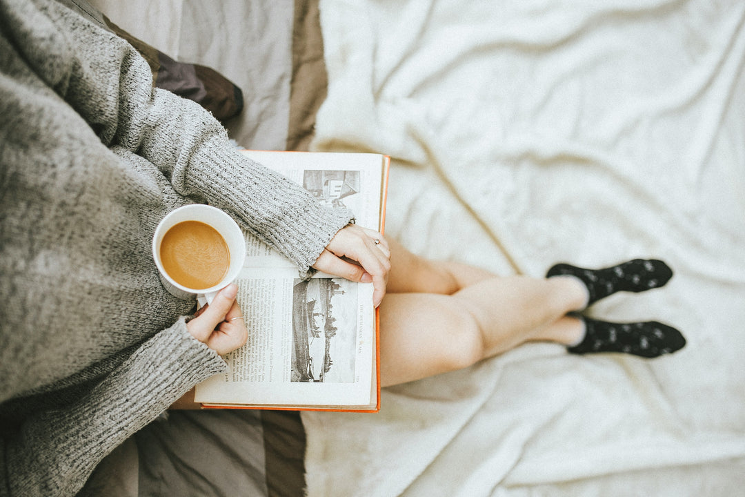 Woman in a Cosy Book Nook reading with a coffee surrounded by blankets