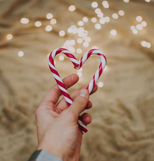 candy canes held out by a hand, over a bakcdrop of beige ruffled material and fairy lights twinkling in the background