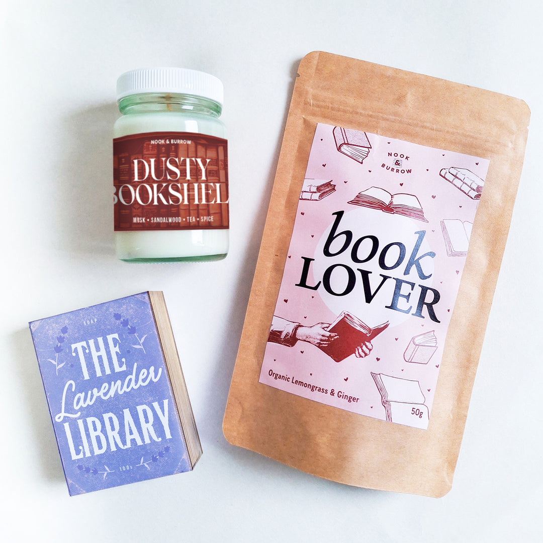 Bookish bundle with “Book Lover” lemongrass and ginger tea, “Dusty Bookshelf” candle, and “The Lavender Library” soap in pastel tones.